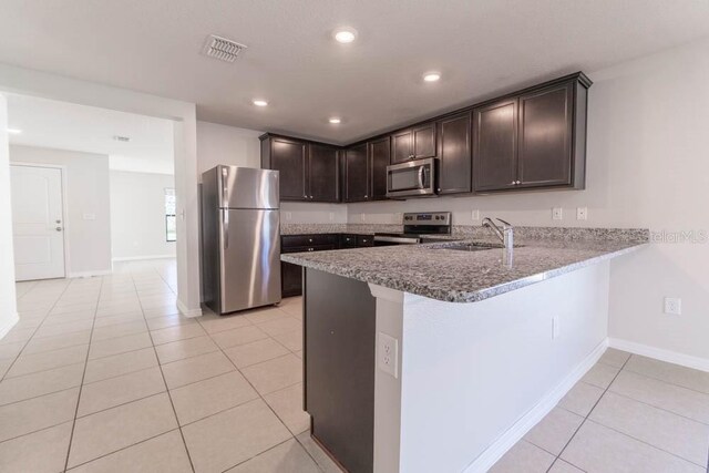 kitchen with appliances with stainless steel finishes, light tile patterned flooring, sink, dark brown cabinets, and kitchen peninsula