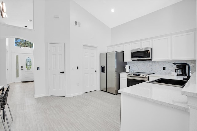 kitchen featuring sink, white cabinetry, appliances with stainless steel finishes, light stone counters, and high vaulted ceiling