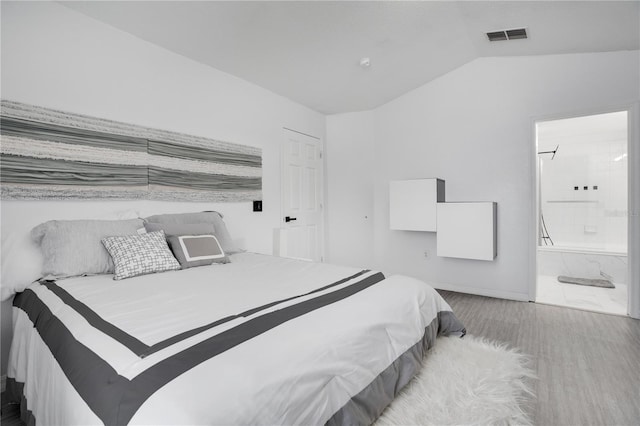 bedroom with connected bathroom, light hardwood / wood-style floors, and vaulted ceiling