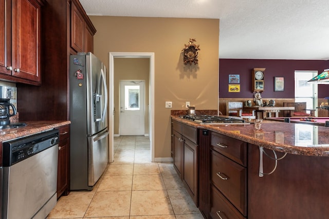 kitchen featuring dark stone countertops, light tile patterned floors, a textured ceiling, kitchen peninsula, and stainless steel appliances