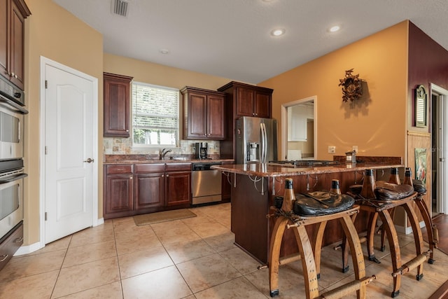 kitchen featuring dark stone counters, a kitchen breakfast bar, decorative backsplash, light tile patterned floors, and appliances with stainless steel finishes