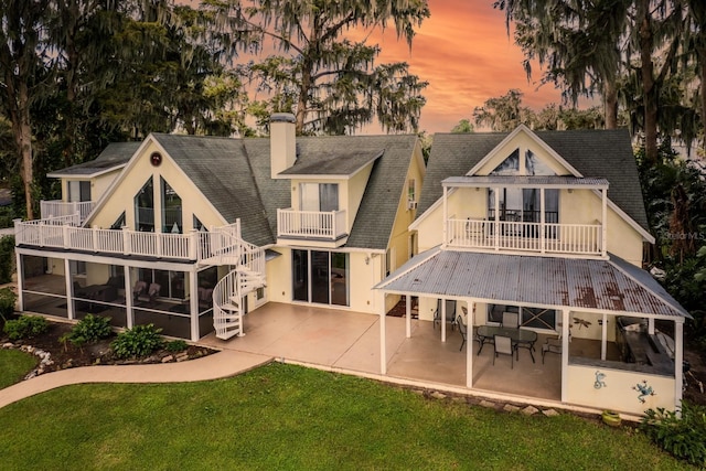 back house at dusk with a balcony, a yard, and a patio