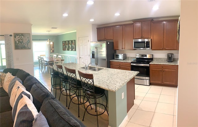 kitchen with light tile patterned floors, an island with sink, stainless steel appliances, sink, and decorative light fixtures