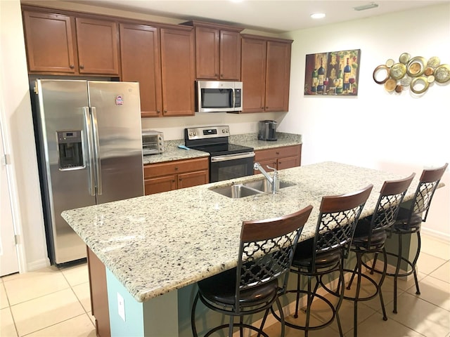 kitchen with appliances with stainless steel finishes, light tile patterned flooring, sink, a kitchen breakfast bar, and a kitchen island with sink