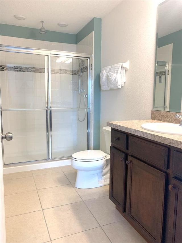 bathroom featuring vanity, toilet, a shower with shower door, and tile patterned flooring