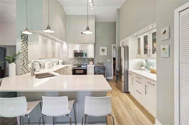 kitchen with a high ceiling, kitchen peninsula, sink, a breakfast bar, and appliances with stainless steel finishes