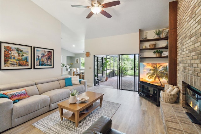 living room featuring light hardwood / wood-style flooring, high vaulted ceiling, a fireplace, and ceiling fan