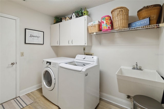 laundry room with washer and dryer, light hardwood / wood-style flooring, sink, a textured ceiling, and cabinets