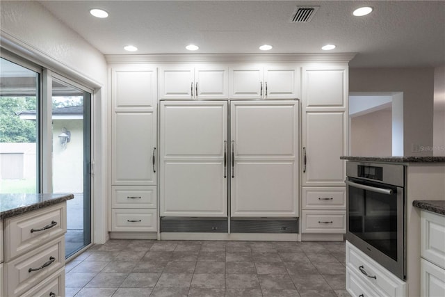 kitchen with oven, paneled built in refrigerator, a textured ceiling, white cabinetry, and dark stone counters