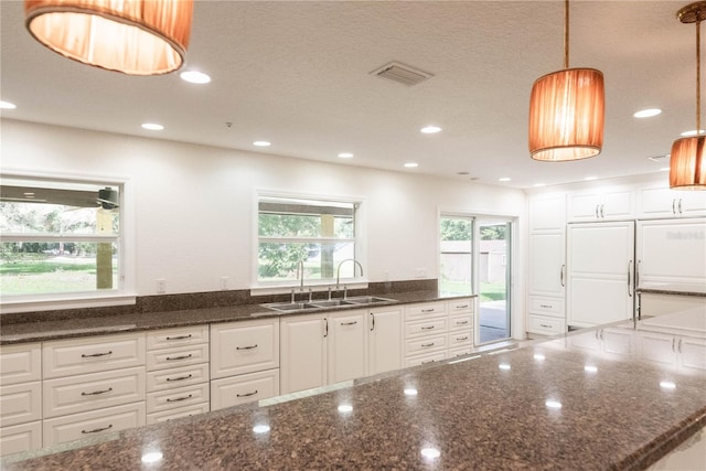 kitchen with sink, white cabinetry, pendant lighting, and dark stone countertops