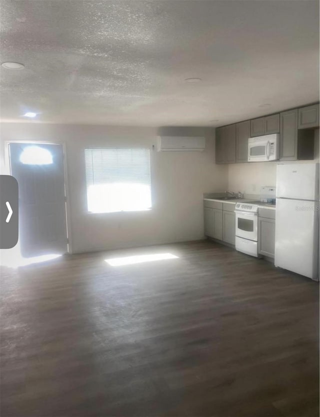 kitchen with a textured ceiling, dark hardwood / wood-style floors, an AC wall unit, gray cabinetry, and white appliances