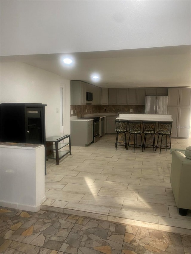 kitchen featuring gray cabinetry, a kitchen bar, a kitchen island, stainless steel appliances, and decorative backsplash