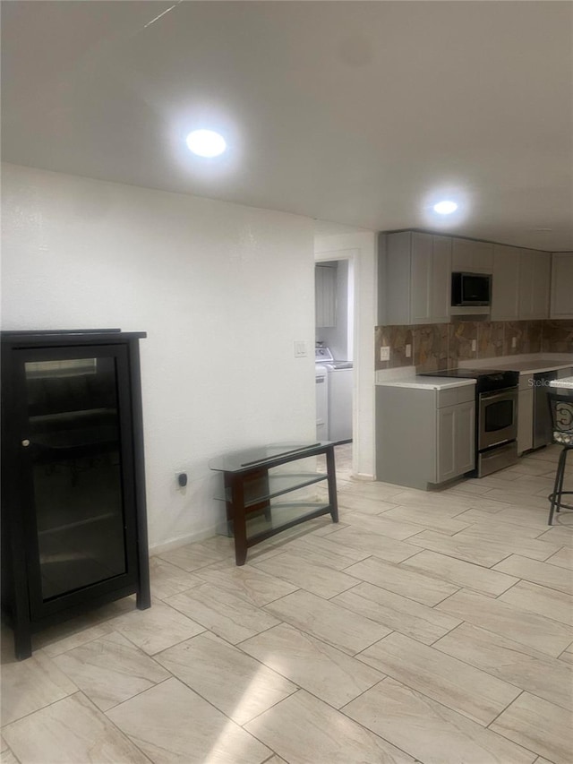 kitchen with decorative backsplash, stainless steel appliances, washer and clothes dryer, and gray cabinetry