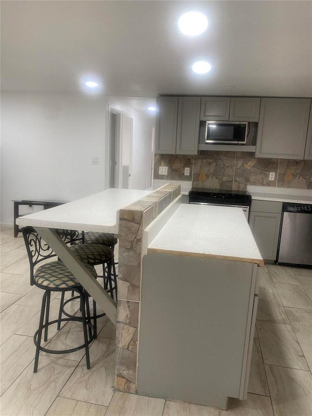 kitchen featuring a breakfast bar, decorative backsplash, stainless steel appliances, and gray cabinetry