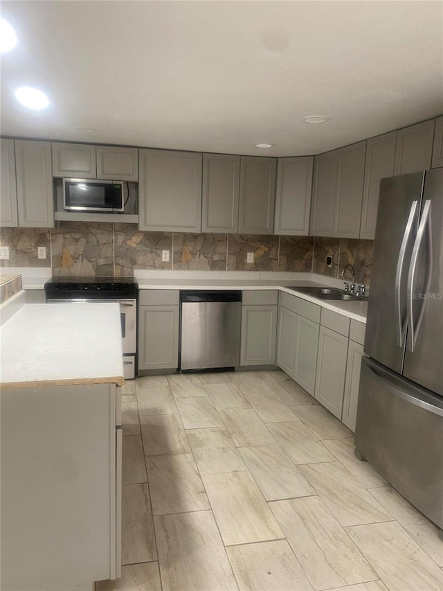 kitchen with appliances with stainless steel finishes, gray cabinetry, sink, and backsplash