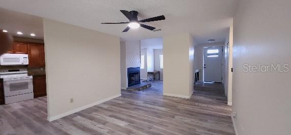 interior space featuring white appliances, a ceiling fan, baseboards, and wood finished floors