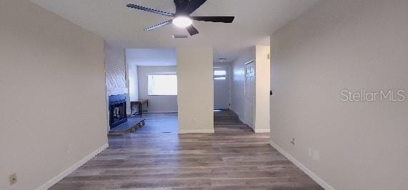 interior space featuring baseboards, ceiling fan, a fireplace, and wood finished floors
