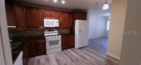 kitchen with light wood-style floors, dark countertops, decorative backsplash, and white appliances