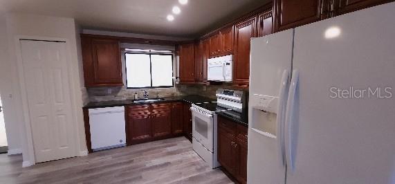 kitchen with dark countertops, a sink, light wood finished floors, white appliances, and backsplash