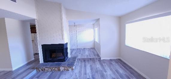 unfurnished living room with visible vents, a fireplace with raised hearth, baseboards, and wood finished floors