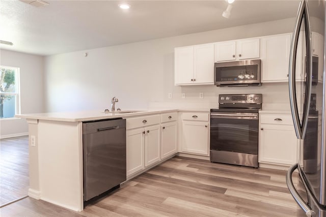 kitchen featuring kitchen peninsula, appliances with stainless steel finishes, white cabinetry, light hardwood / wood-style flooring, and sink