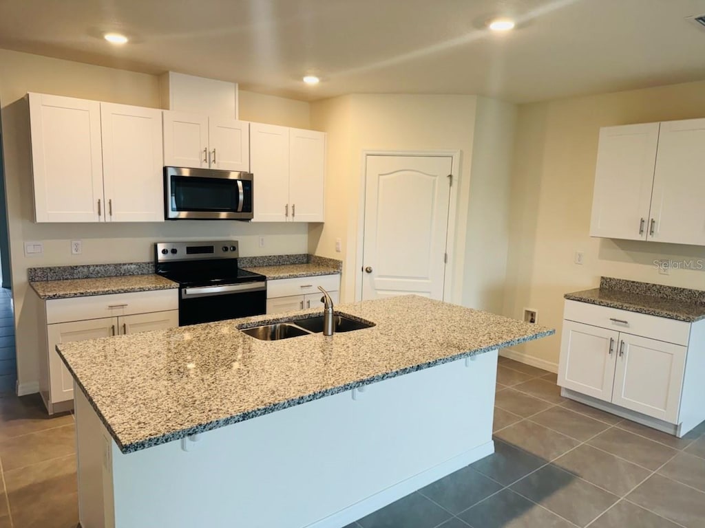 kitchen with sink, white cabinetry, dark tile patterned floors, range with electric stovetop, and an island with sink