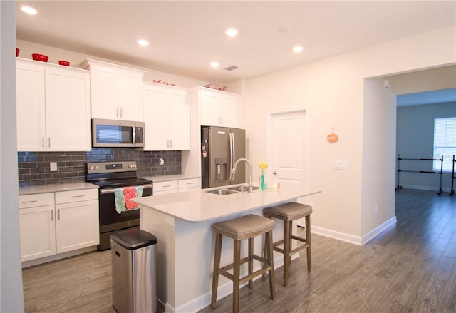 kitchen featuring wood-type flooring, sink, an island with sink, stainless steel appliances, and white cabinets