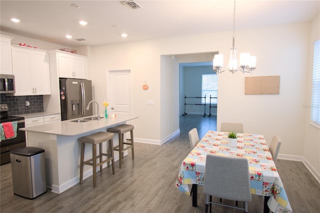 kitchen featuring appliances with stainless steel finishes, dark hardwood / wood-style floors, decorative light fixtures, and an island with sink