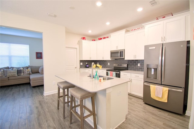 kitchen with appliances with stainless steel finishes, a kitchen breakfast bar, white cabinetry, light hardwood / wood-style flooring, and a center island with sink