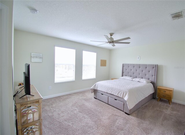 bedroom with ceiling fan, light carpet, and a textured ceiling