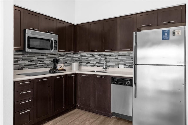 kitchen featuring dark brown cabinets, sink, light wood-type flooring, appliances with stainless steel finishes, and tasteful backsplash