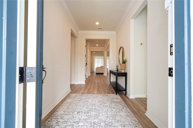 corridor with light hardwood / wood-style floors and ornamental molding