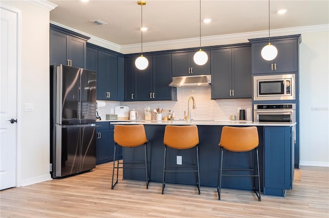 kitchen featuring appliances with stainless steel finishes, ornamental molding, a kitchen island with sink, and decorative light fixtures