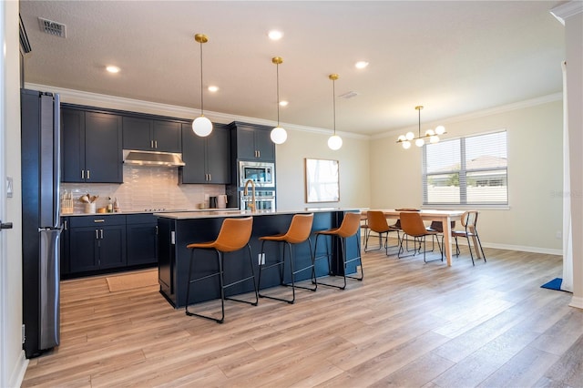 kitchen featuring a kitchen breakfast bar, stainless steel appliances, pendant lighting, light hardwood / wood-style flooring, and a kitchen island with sink