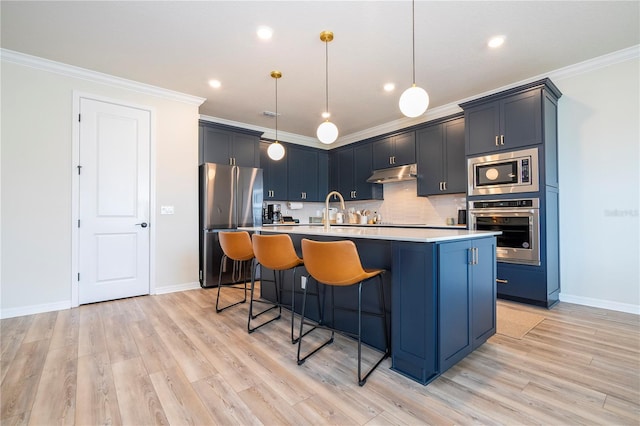 kitchen featuring hanging light fixtures, appliances with stainless steel finishes, a kitchen breakfast bar, a kitchen island with sink, and light hardwood / wood-style floors