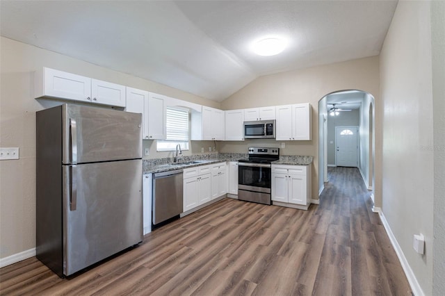 kitchen with stainless steel appliances, light stone countertops, white cabinets, dark wood-type flooring, and vaulted ceiling