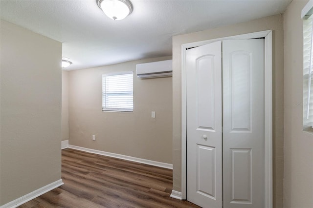 unfurnished bedroom featuring a closet, a wall unit AC, and dark hardwood / wood-style floors