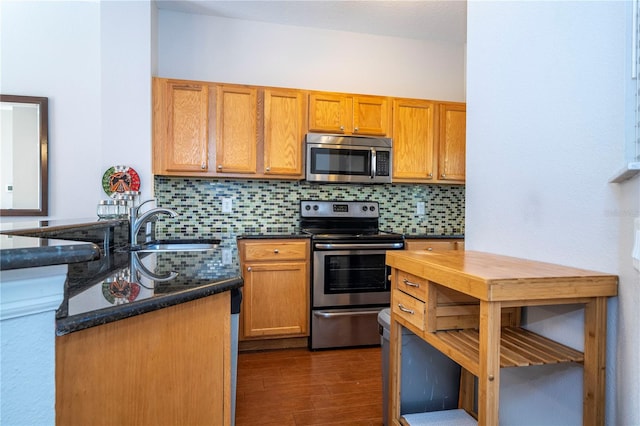 kitchen with appliances with stainless steel finishes, sink, backsplash, dark stone counters, and dark wood-type flooring