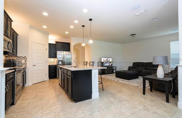 kitchen featuring a kitchen breakfast bar, hanging light fixtures, stainless steel appliances, a center island with sink, and crown molding