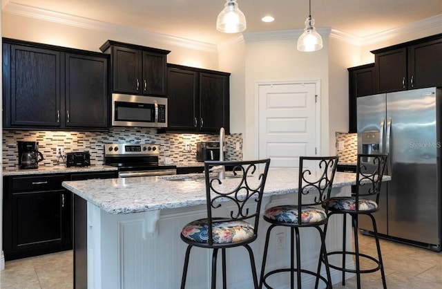 kitchen featuring hanging light fixtures, appliances with stainless steel finishes, ornamental molding, and a kitchen island with sink