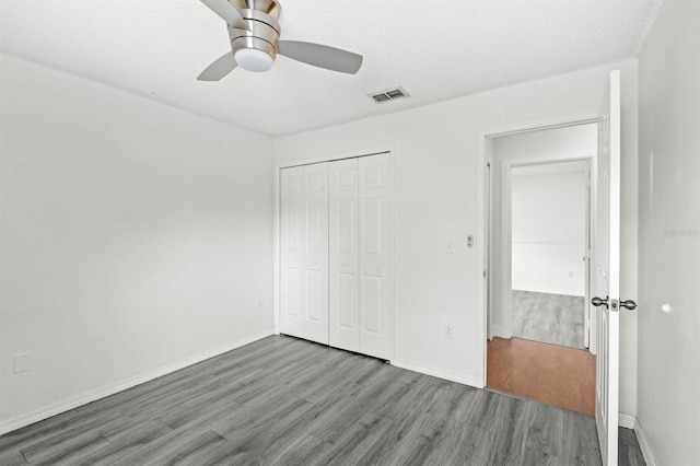 unfurnished bedroom featuring a closet, ceiling fan, wood-type flooring, and a textured ceiling