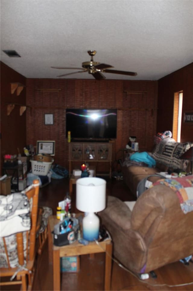 living room featuring ceiling fan, a textured ceiling, and wooden walls