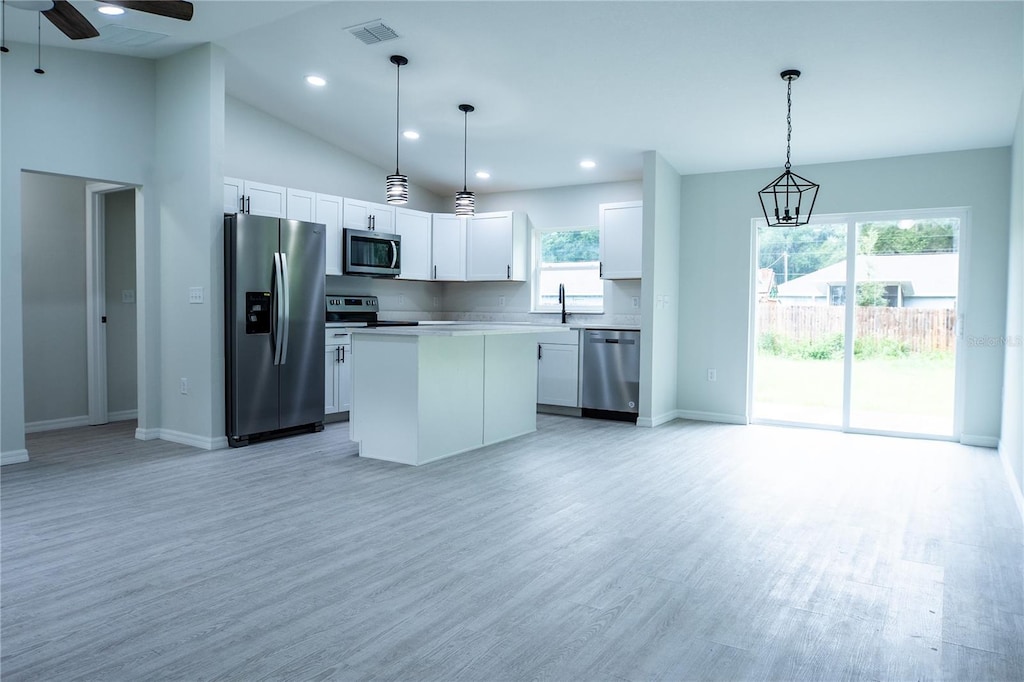 kitchen with white cabinets, light wood-type flooring, stainless steel appliances, decorative light fixtures, and a center island