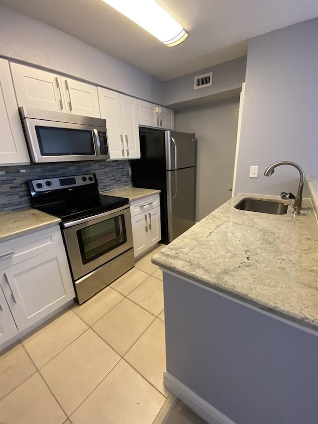 kitchen with white cabinets, tasteful backsplash, light stone counters, sink, and stainless steel appliances