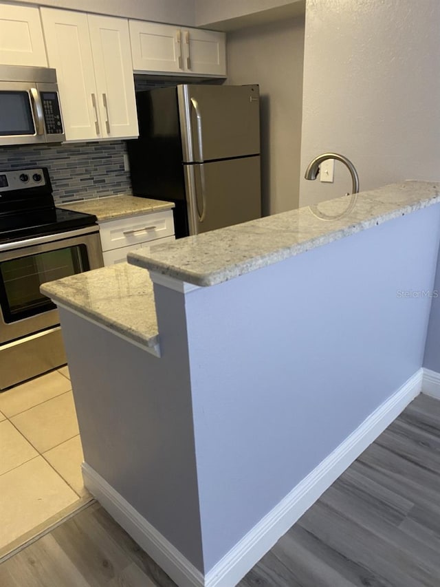 kitchen with tasteful backsplash, appliances with stainless steel finishes, white cabinets, light stone counters, and light hardwood / wood-style flooring