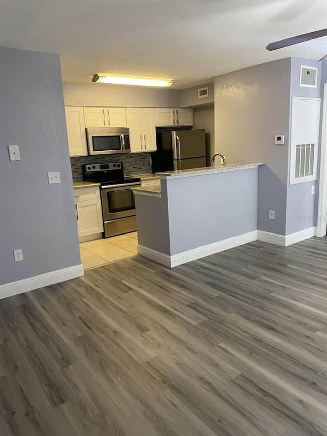 kitchen featuring decorative backsplash, white cabinetry, stainless steel appliances, and hardwood / wood-style flooring