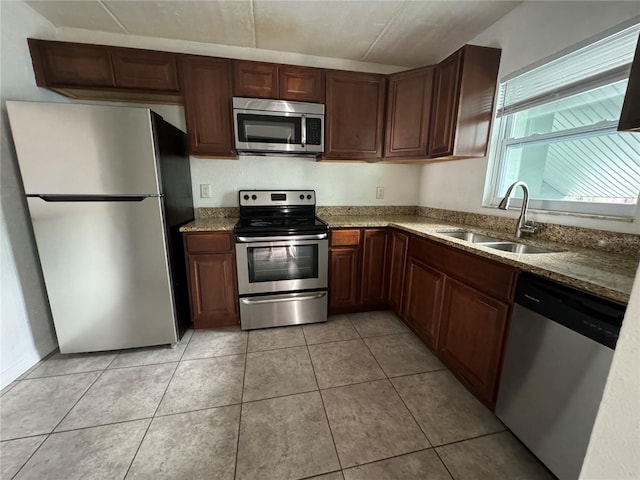 kitchen featuring appliances with stainless steel finishes, light stone counters, light tile patterned floors, and sink