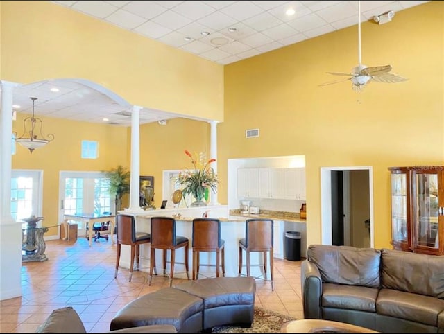 living room with ornate columns, ceiling fan, a towering ceiling, and light tile patterned floors