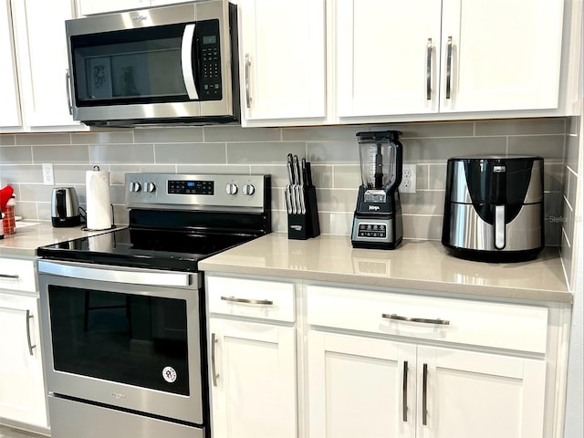 kitchen with appliances with stainless steel finishes, white cabinets, light stone countertops, and tasteful backsplash