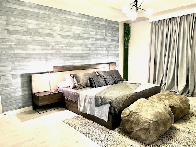 bedroom featuring wooden walls, light hardwood / wood-style flooring, and an inviting chandelier